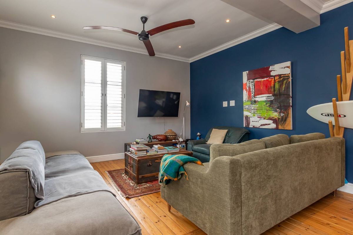 A comfortable living room featuring polished timber flooring, recessed downlighting, a ceiling fan, and plantation shutters.