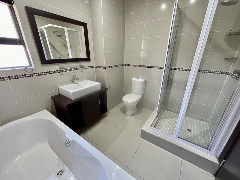 A modern, well-maintained bathroom featuring a bathtub, separate shower enclosure, vanity basin, and toilet with neutral floor-to-ceiling tiling.