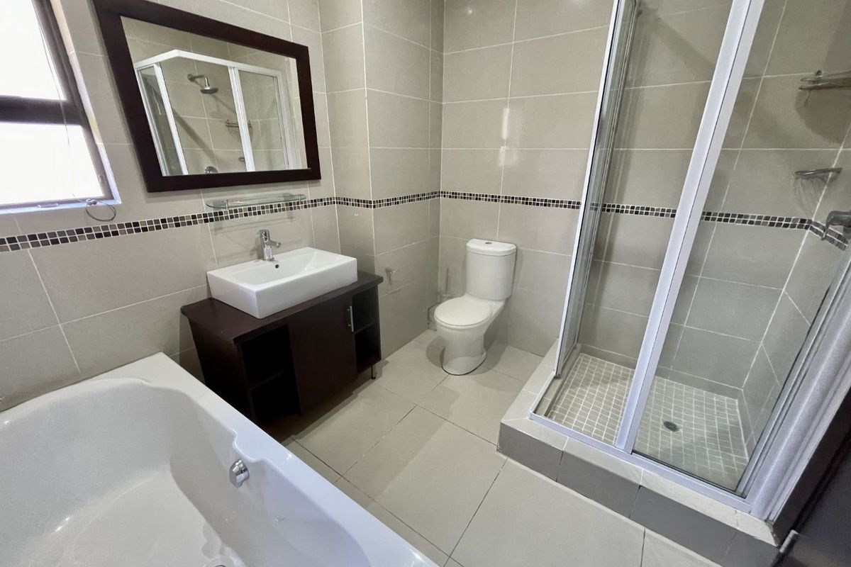 A modern, well-maintained bathroom featuring a bathtub, separate shower enclosure, vanity basin, and toilet with neutral floor-to-ceiling tiling.