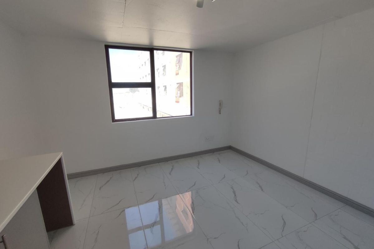 A bright, empty bedroom featuring modern marble-look floor tiles, a large window, and a built-in desk area.