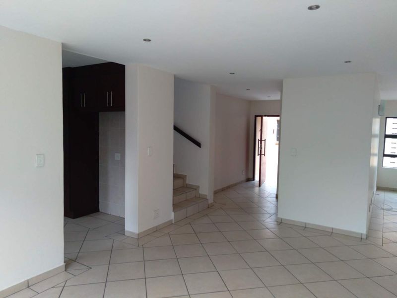 An open-plan living area featuring tiled flooring, recessed downlights, and a staircase leading to the upper level.