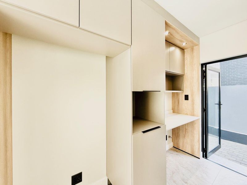A modern, minimalist scullery or utility area featuring sleek built-in cabinetry, wood-look accents, and direct access to an outdoor paved area.
