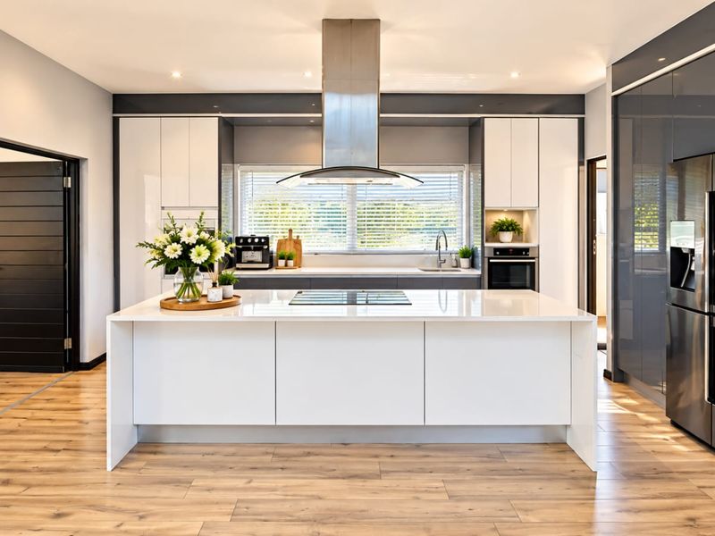 Modern kitchen featuring a central island with quartz countertops, high-gloss cabinetry, stainless steel appliances, and wood-look laminate flooring.