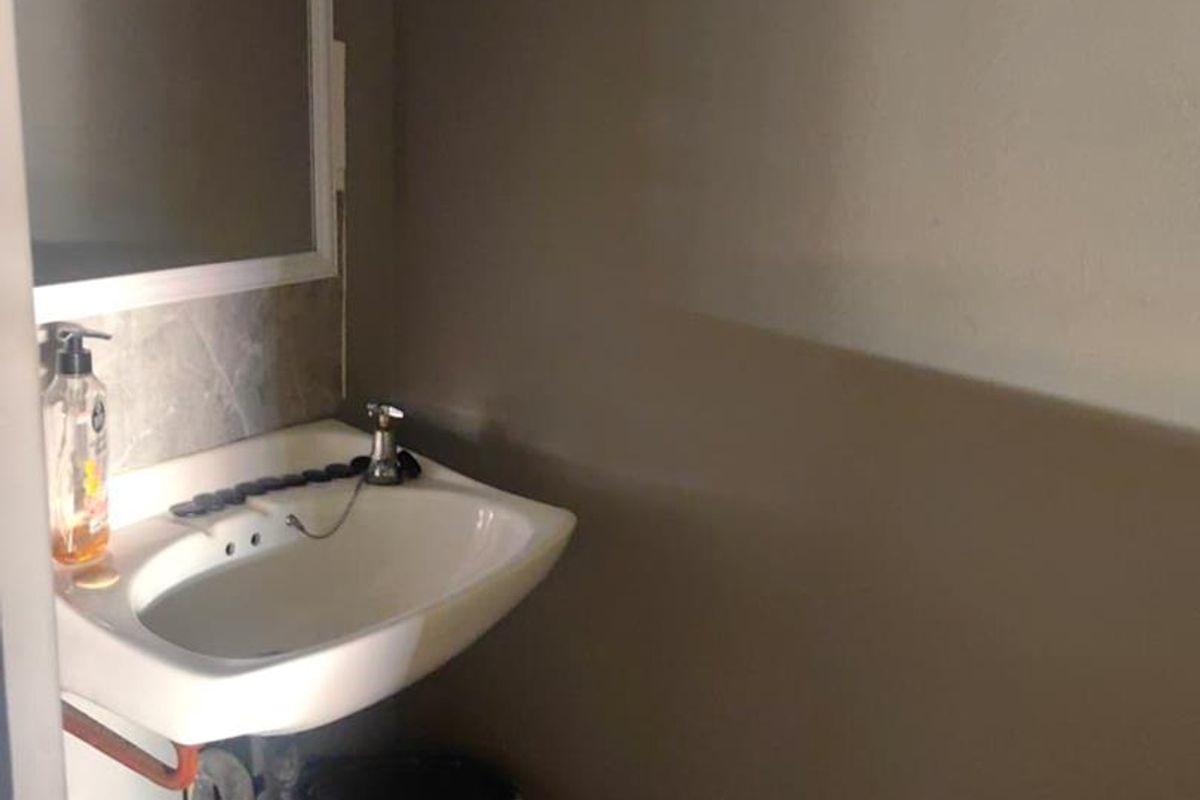 A small bathroom or powder room featuring a wall-mounted basin with exposed plumbing and a simple mirror.