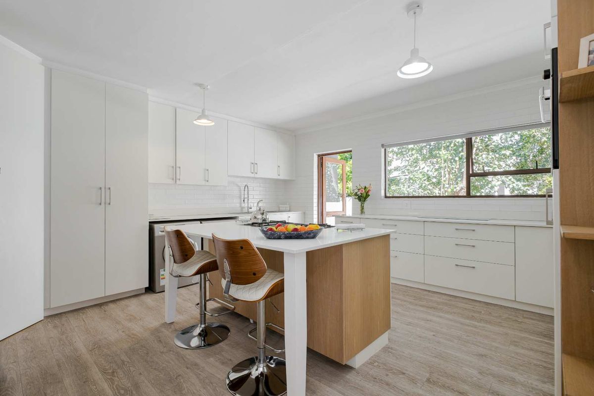Modern kitchen featuring white cabinetry, a central island with wood-look finish, stone countertops, and light wood-look flooring with direct access to the outdoors.