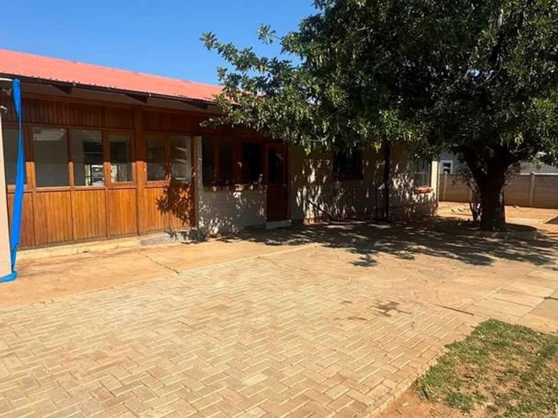 Rear exterior view of the property featuring a paved courtyard area, timber-clad wall sections, and a large mature tree providing shade.