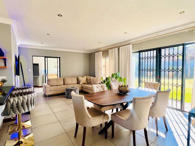 Spacious open-plan living and dining area featuring large format floor tiles, recessed lighting, and direct access to the garden through sliding security doors.
