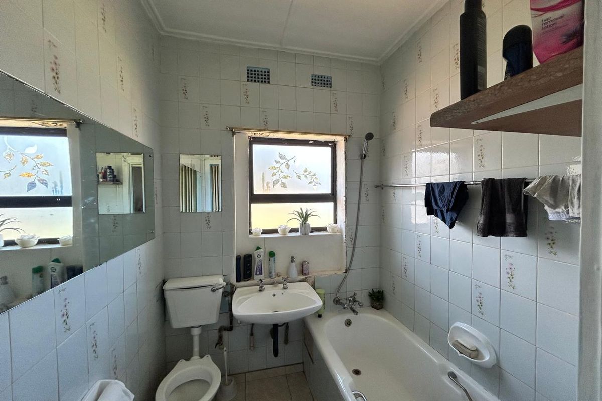 A compact bathroom featuring a standard bathtub, wall-mounted basin, and toilet, finished with dated floral-patterned wall tiles.