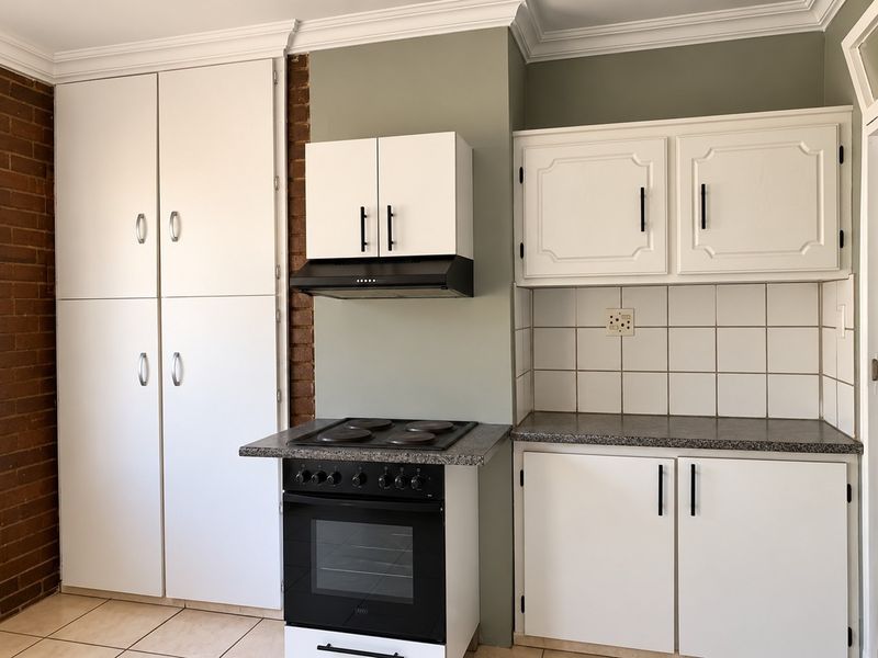 A functional kitchen featuring white cabinetry, an electric stove with extractor fan, tiled backsplash, and a distinctive exposed brick wall.