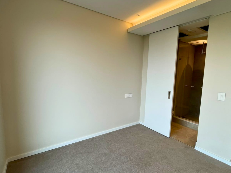 A clean, empty bedroom featuring neutral carpeting, recessed ceiling lighting, and a sliding door providing access to an en-suite bathroom.