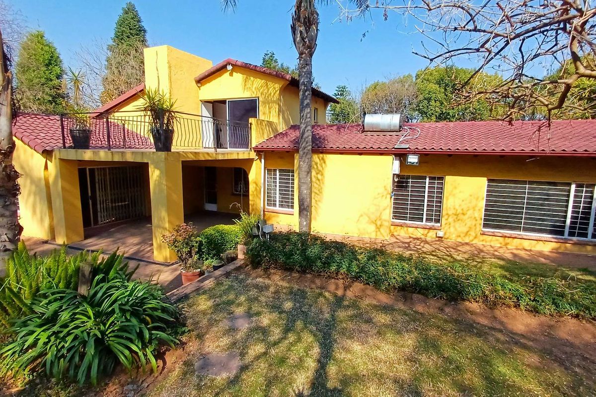 Rear view of a yellow house featuring a tiled roof, solar geyser, upper-level balcony, and a covered patio overlooking the garden.