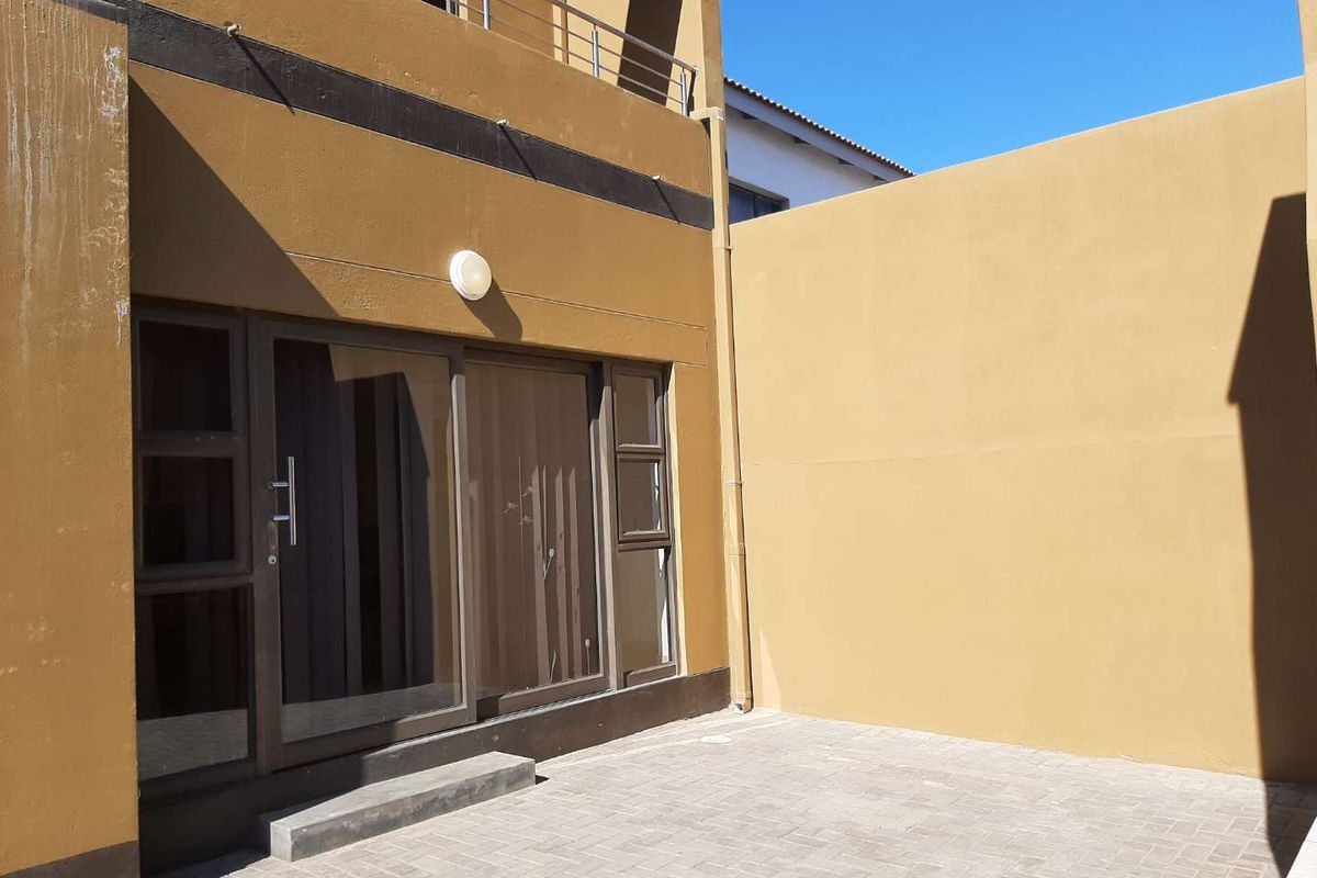 A private rear courtyard featuring paved flooring, a sliding glass door entrance, and a balcony above.