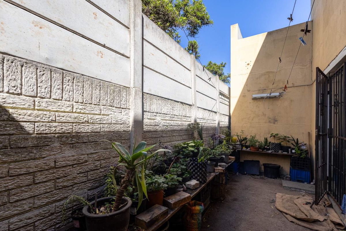 A rear exterior courtyard area featuring a precast concrete boundary wall and a security gate, offering potential for landscaping or outdoor improvement.