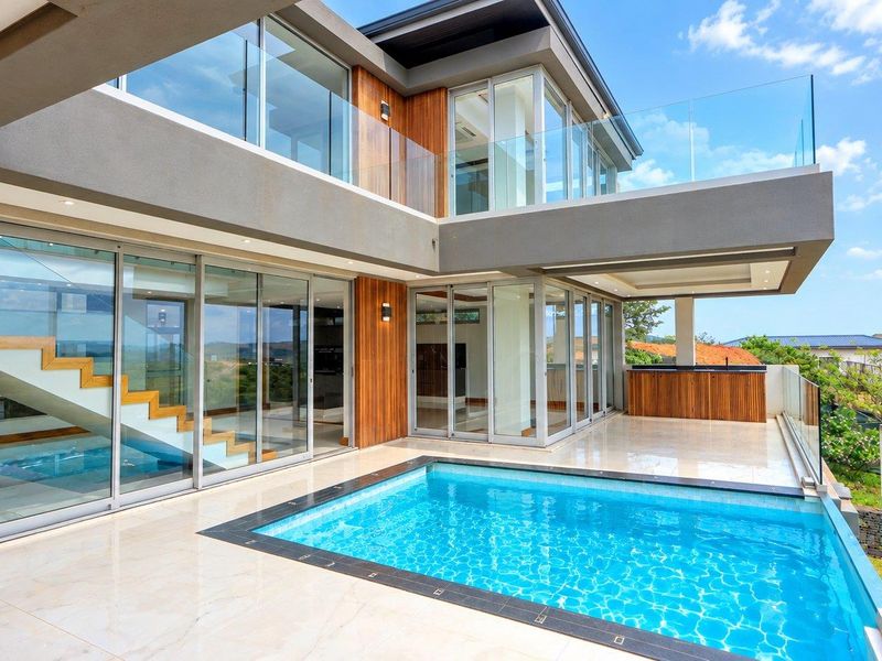 Modern luxury outdoor living area featuring a swimming pool, tiled patio, glass balustrades, and seamless indoor-outdoor flow through large sliding glass doors.