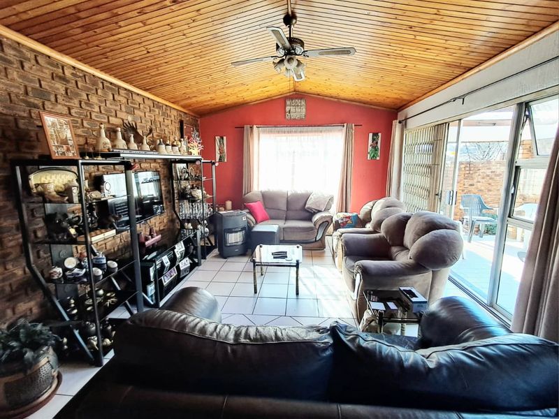 Spacious living room featuring an exposed brick wall, timber-clad vaulted ceiling with a fan, and large sliding doors providing access to the patio.