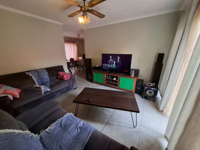 A comfortable living room featuring tiled flooring and a ceiling fan, with an open-plan layout leading towards the dining area.