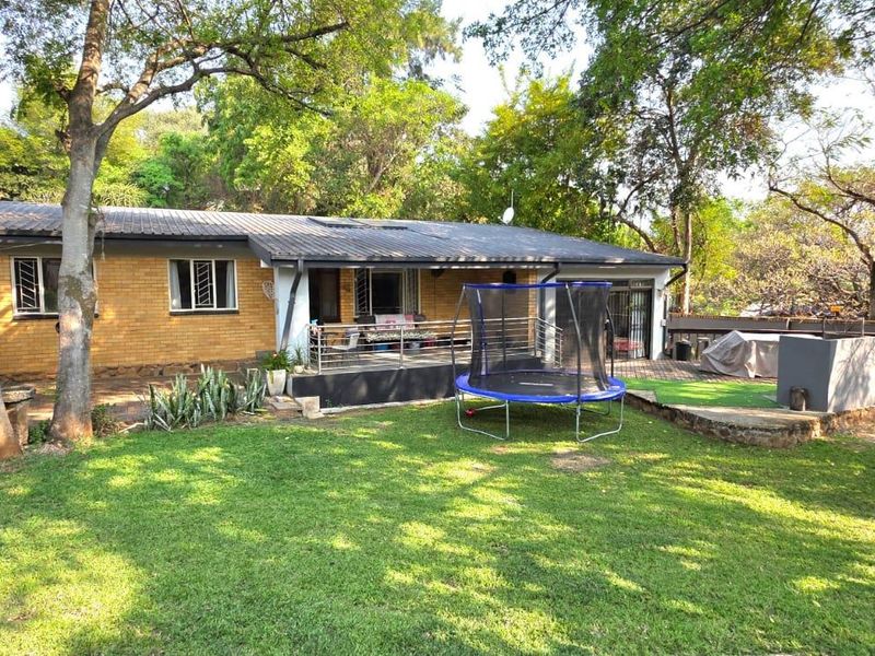 Rear view of the property featuring a brick facade, corrugated roof, paved patio area, and a raised timber deck overlooking the garden.