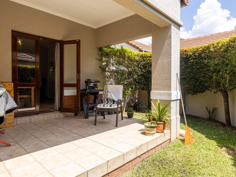 A covered patio area with tiled flooring, providing direct access to the garden through double glass doors.