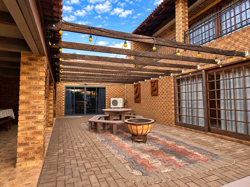 A spacious outdoor patio area featuring a timber pergola, brick paving, and direct access to the home through sliding glass doors.