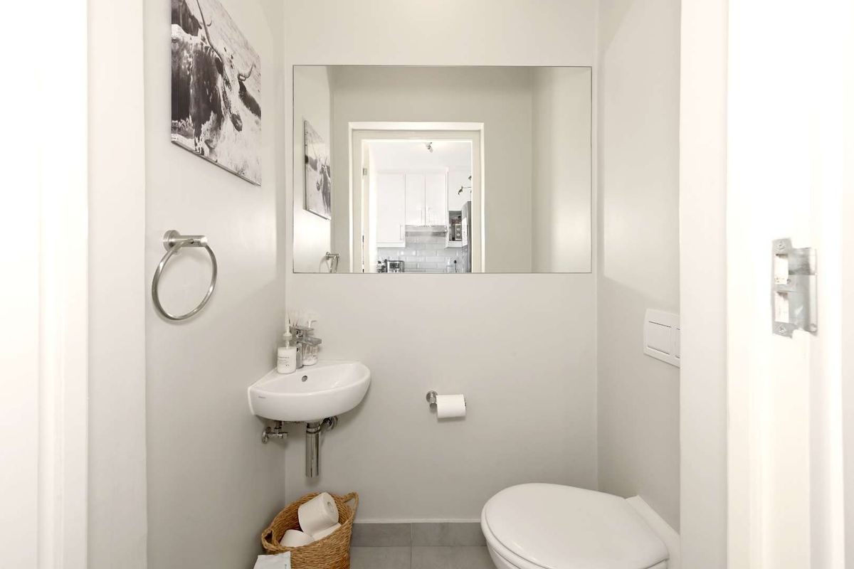 A compact guest bathroom featuring a wall-mounted corner basin, a large frameless mirror, and a modern toilet.