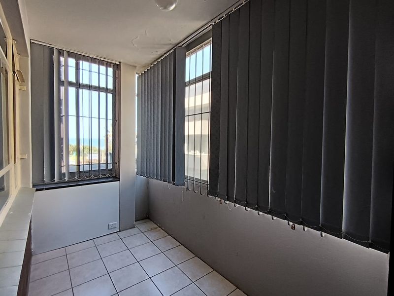 Enclosed balcony area featuring tiled flooring, security bars on windows, and vertical blinds, offering a functional space with potential for modernization.