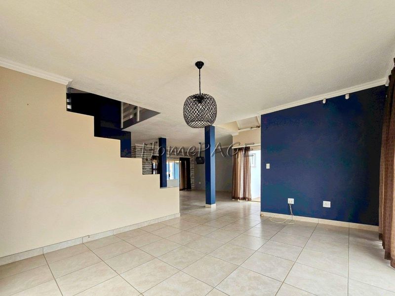 Spacious open-plan living area featuring tiled flooring, a central staircase, and modern pendant lighting, offering a versatile layout for interior design.