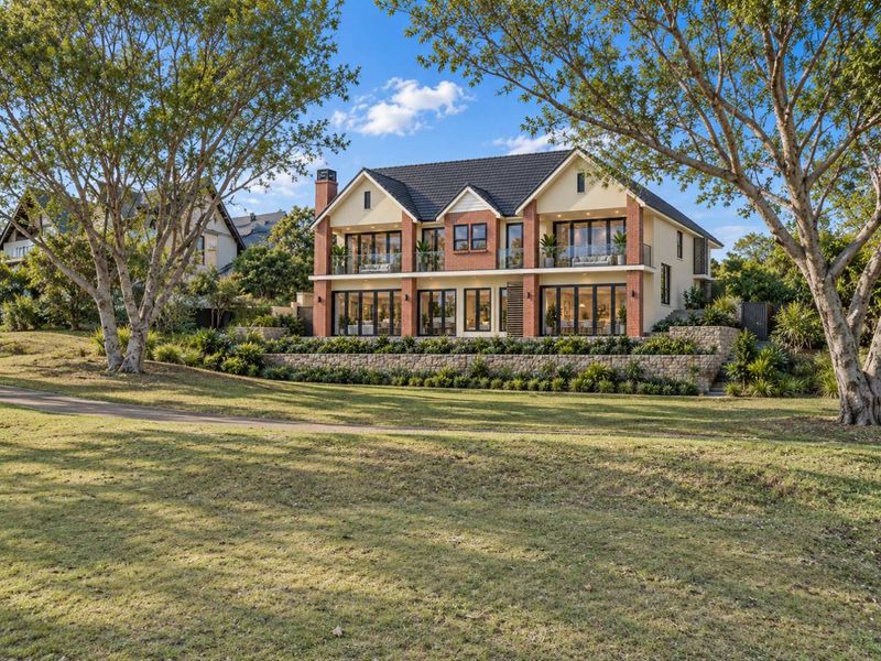 A stunning two-story residential property featuring a brick and render facade, stone retaining walls, and expansive glass doors opening onto balconies.