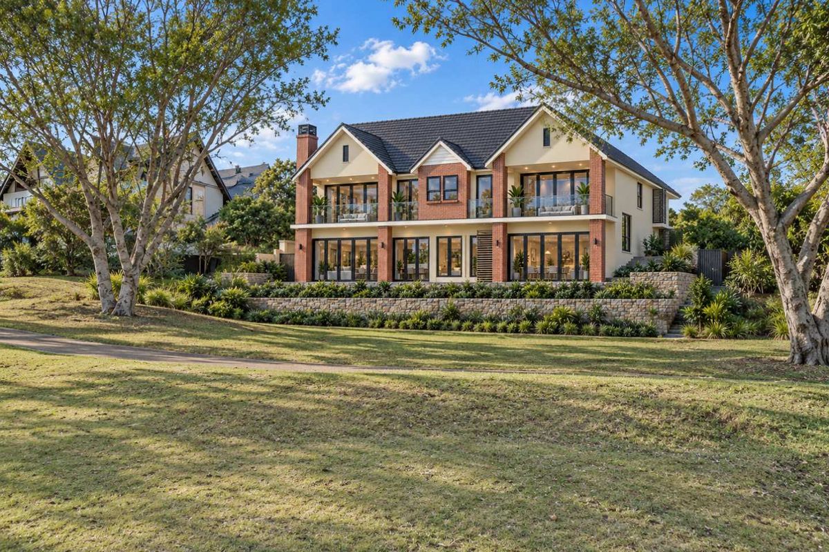 A stunning two-story residential property featuring a brick and render facade, stone retaining walls, and expansive glass doors opening onto balconies.