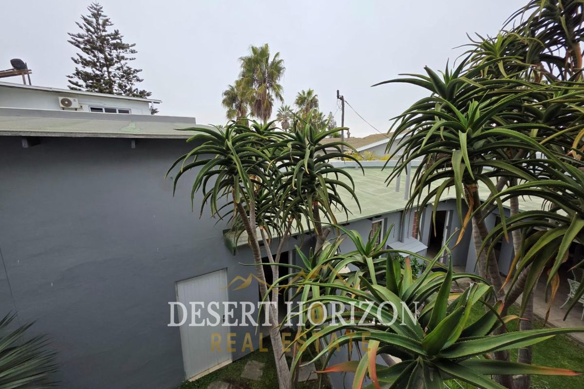An elevated view of the property's exterior, showcasing the building's grey facade, green roof sections, and established garden landscaping.