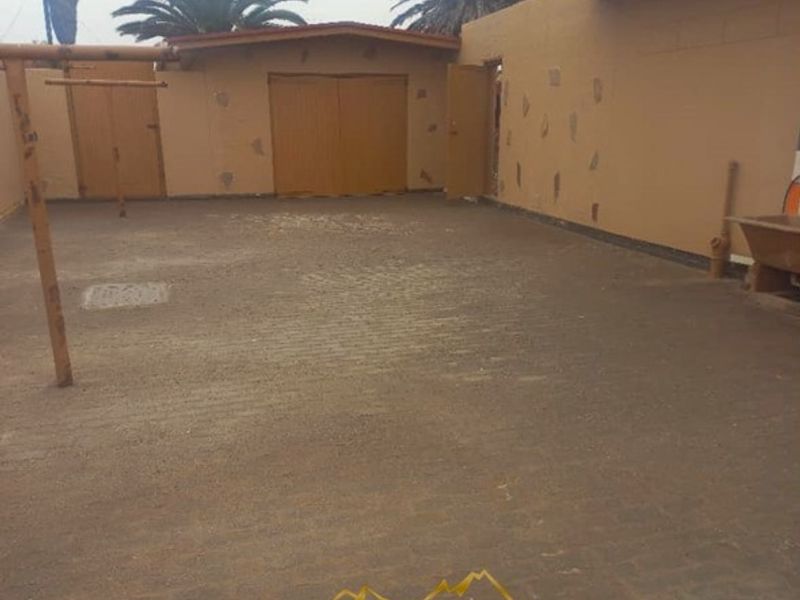 A spacious rear courtyard featuring paved flooring and access to a garage, requiring some exterior maintenance and cosmetic updates.
