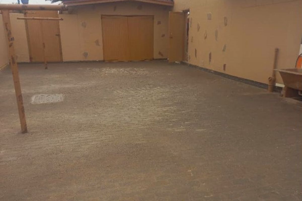 A spacious rear courtyard featuring paved flooring and access to a garage, requiring some exterior maintenance and cosmetic updates.