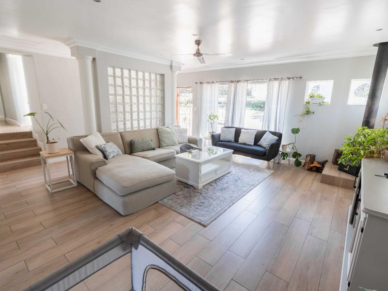 Spacious living room featuring wood-look tile flooring, a feature glass block wall, decorative columns, and a modern freestanding fireplace.