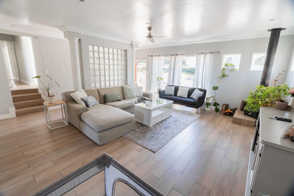 Spacious living room featuring wood-look tile flooring, a feature glass block wall, decorative columns, and a modern freestanding fireplace.
