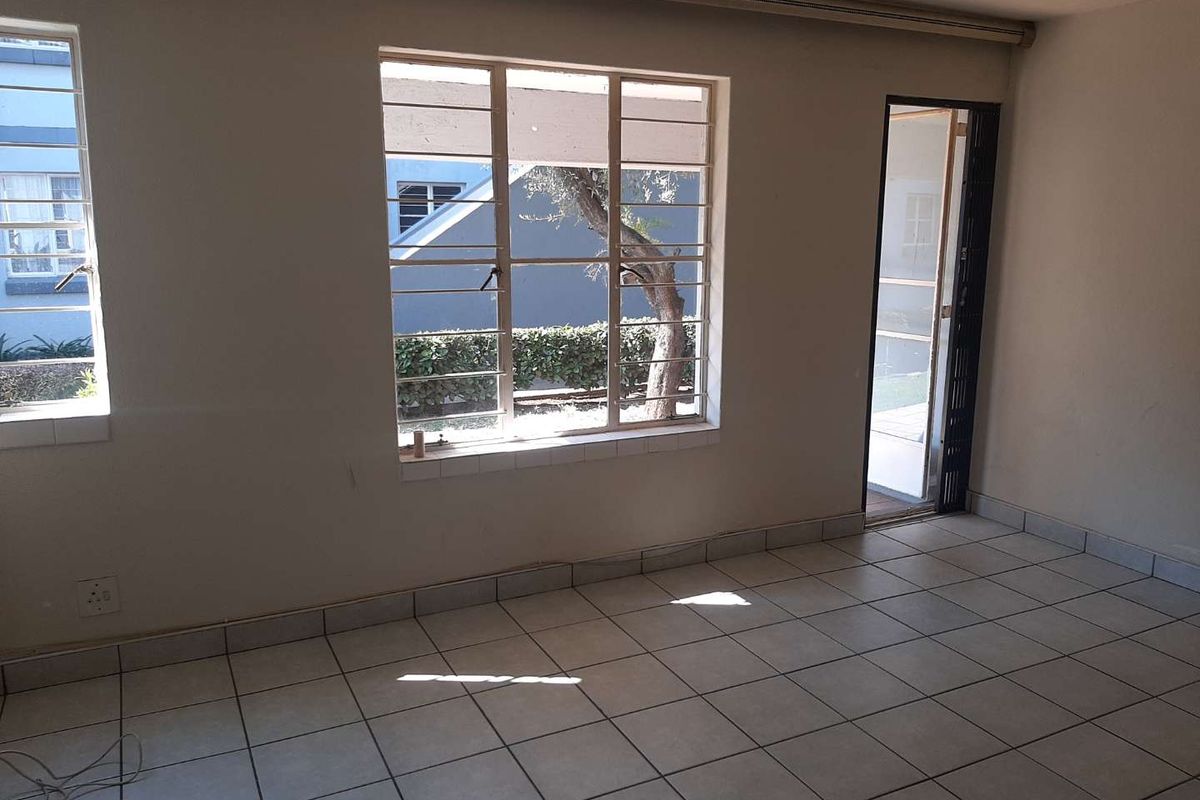 An empty living room featuring tiled flooring, security bars on the windows, and a security gate leading to the exterior.