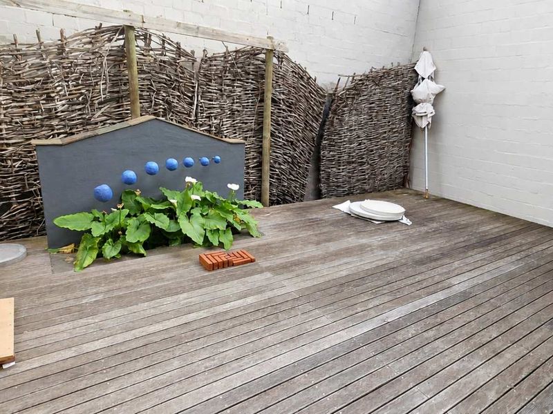 A private outdoor patio area featuring timber decking, a painted feature wall, and natural wattle fencing, offering a versatile space for office breakout or relaxation.