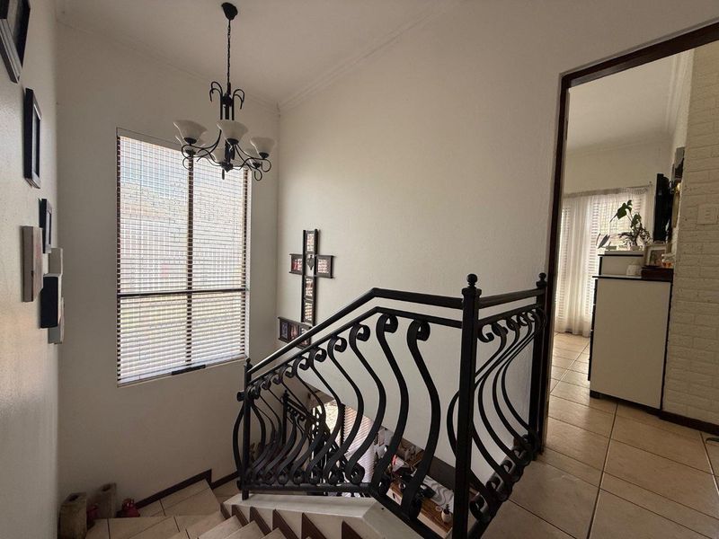 A bright hallway featuring a decorative wrought iron staircase railing, tiled flooring, and a classic chandelier, leading into an adjacent living space.
