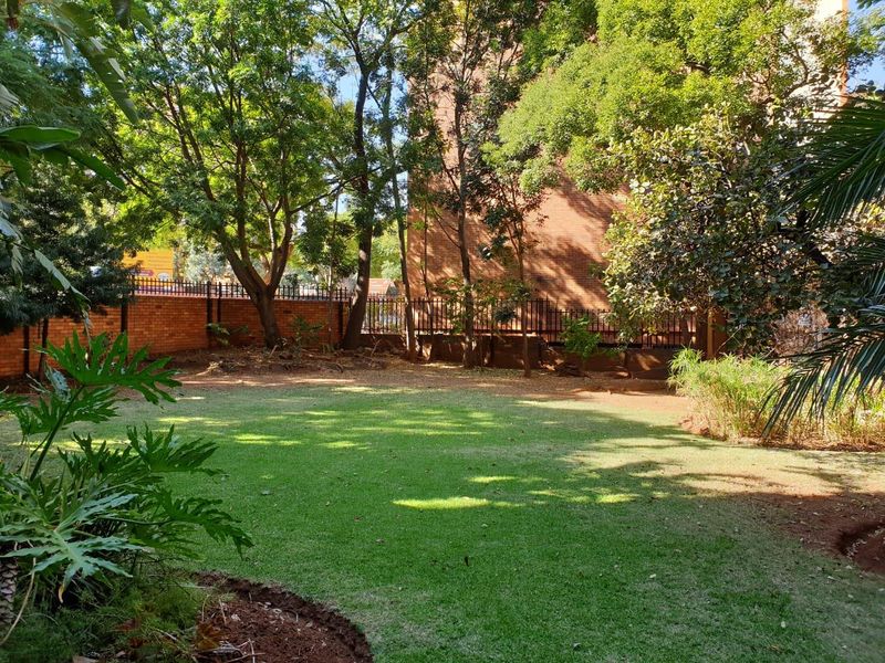 A well-maintained private garden area featuring a lush lawn, mature trees, and secure brick and metal boundary fencing.