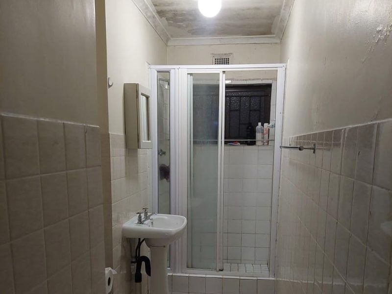 A compact bathroom featuring a pedestal basin, shower enclosure, and tiled finishes, currently requiring maintenance and cosmetic updates to the ceiling and wall surfaces.