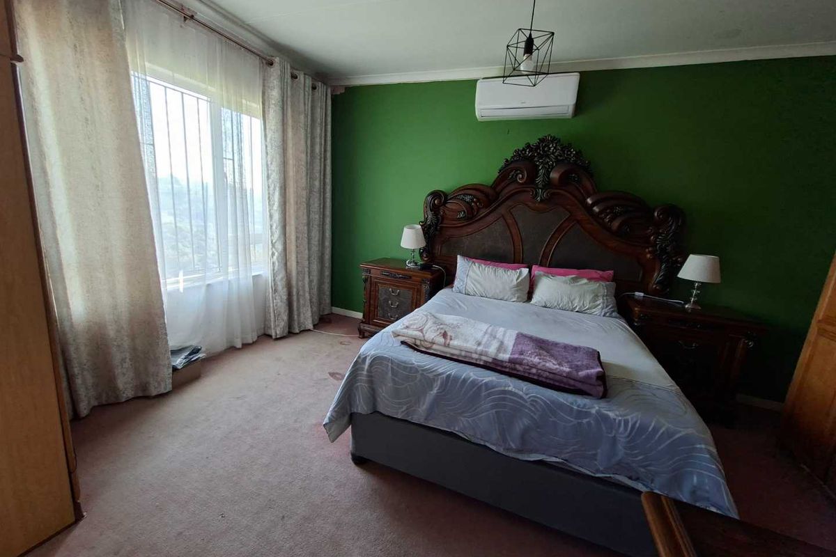 A spacious bedroom featuring a split-system air conditioner, large window with security bars, and carpeted flooring.