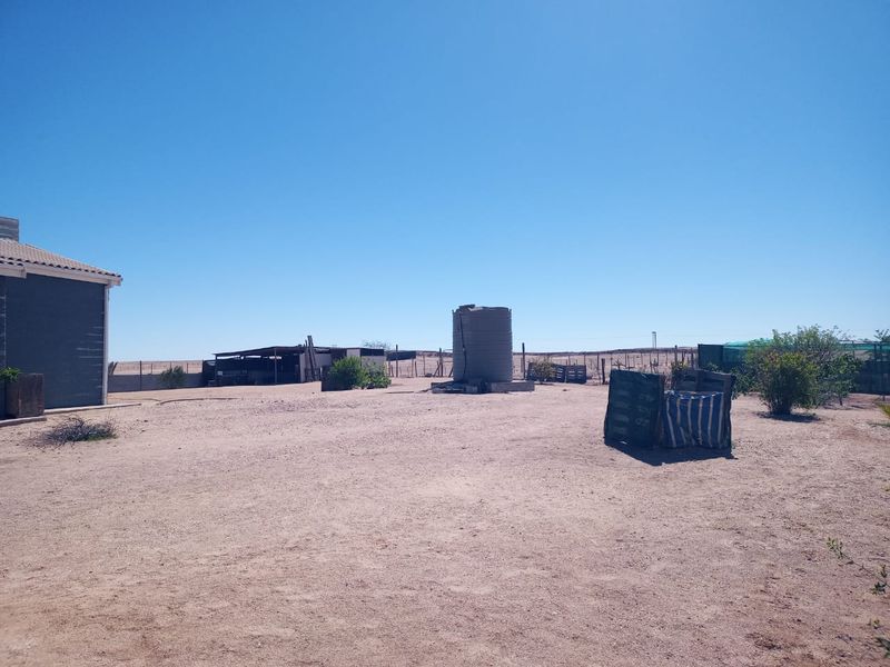 Expansive rear yard area featuring a water storage tank, perimeter fencing, and a small outbuilding structure on a dry, open plot.