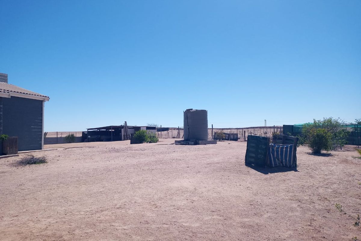Expansive rear yard area featuring a water storage tank, perimeter fencing, and a small outbuilding structure on a dry, open plot.