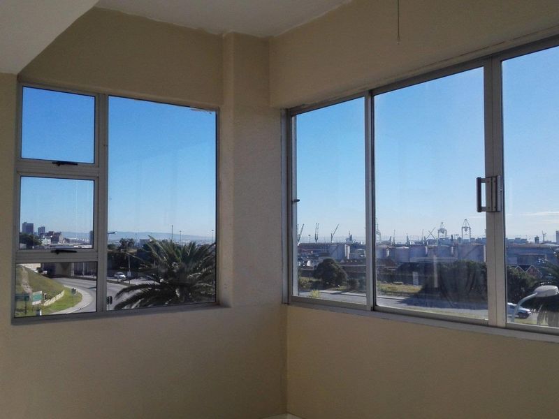 An empty living area featuring large corner windows that provide expansive views of the surrounding industrial landscape and harbour.