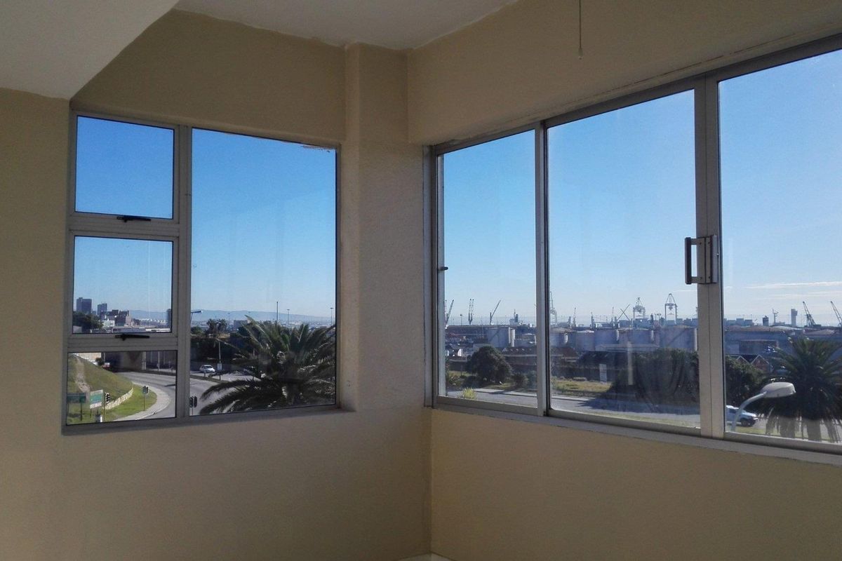 An empty living area featuring large corner windows that provide expansive views of the surrounding industrial landscape and harbour.