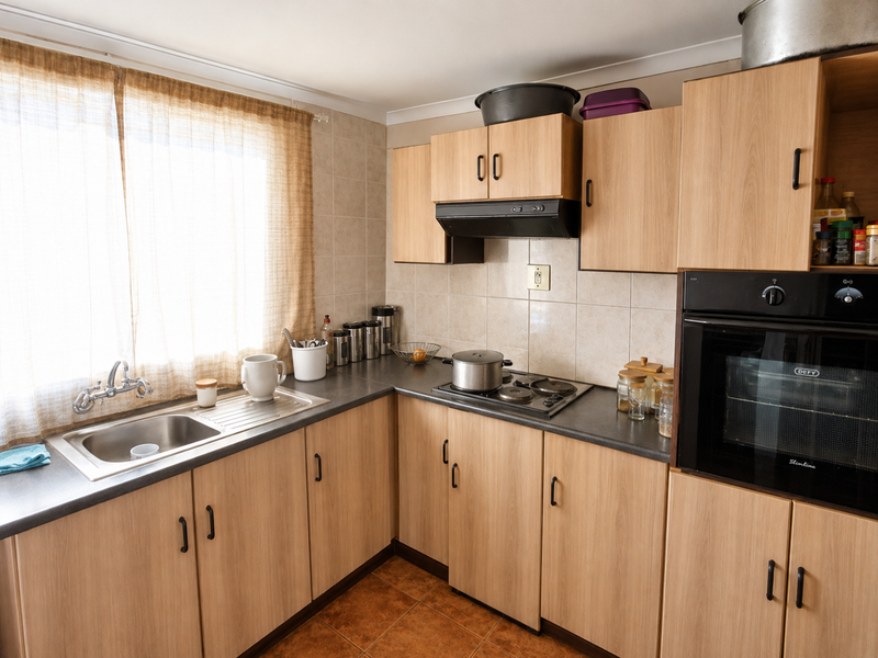 Functional kitchen featuring light wood-look cabinetry, dark laminate countertops, built-in oven, electric hob, and tiled backsplash with natural light.