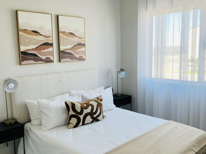 A well-maintained bedroom featuring neutral wall tones, a window with sheer curtains, and a classic tongue and groove ceiling finish.