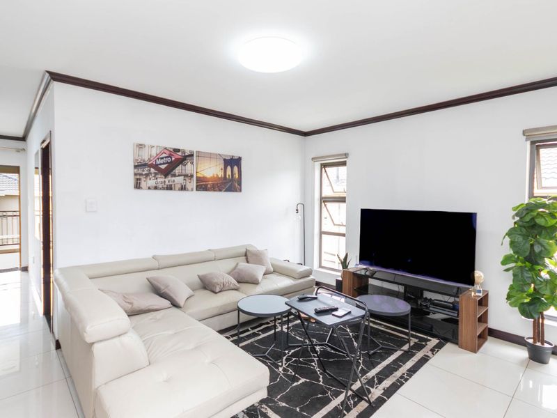 A bright and open living room featuring tiled flooring, dark crown molding, and large windows that provide natural light and access to a balcony.