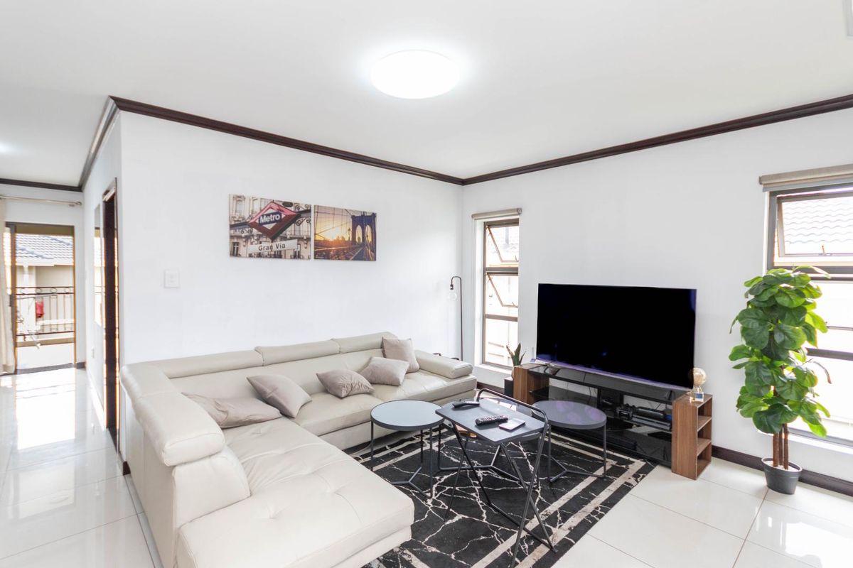 A bright and open living room featuring tiled flooring, dark crown molding, and large windows that provide natural light and access to a balcony.