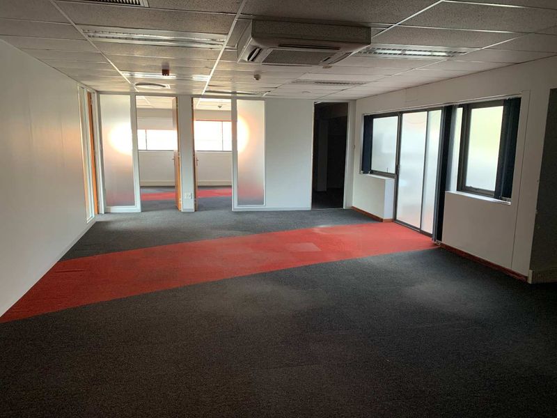 Open plan office space featuring suspended ceiling tiles, integrated air conditioning unit, and glass partition walls with carpeted flooring.
