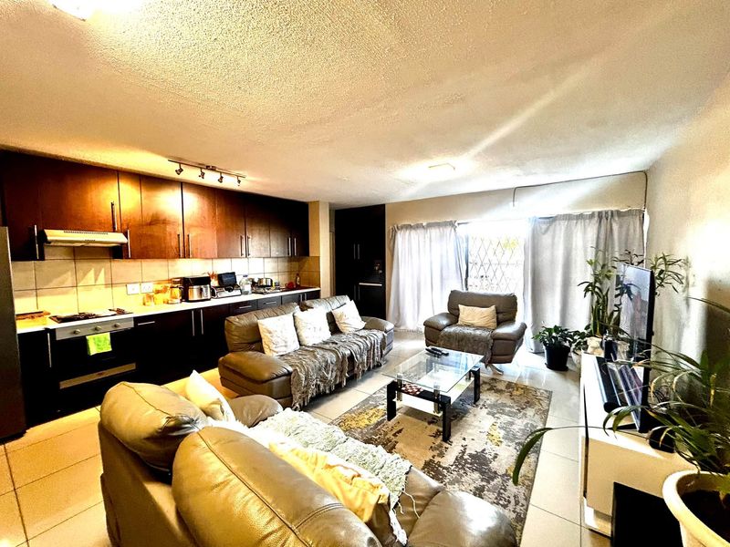 Open plan living area featuring a kitchen with dark cabinetry and tiled flooring, leading to a sliding door with security gate access.