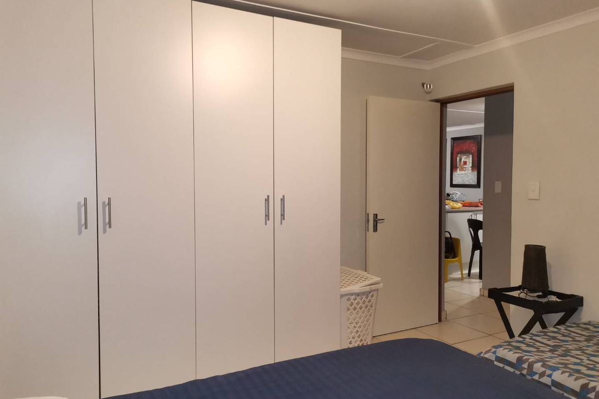 A bedroom featuring built-in white cabinetry and tiled flooring, with a doorway leading to an adjacent living area.
